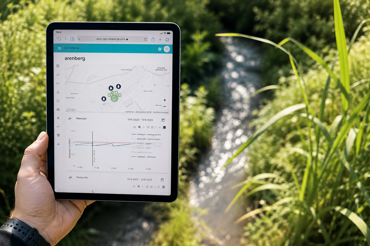 Een tablet in de hand bij de waterloop, met het Sirio-portaal van Sumaqua open op de site Arenberg: een kaart met de meetpunten en een grafiek waarin de sensormeting, de handmeting, de gesimuleerde waterstand en de alarmgrenzen samen staan, met daaronder de pompgegevens